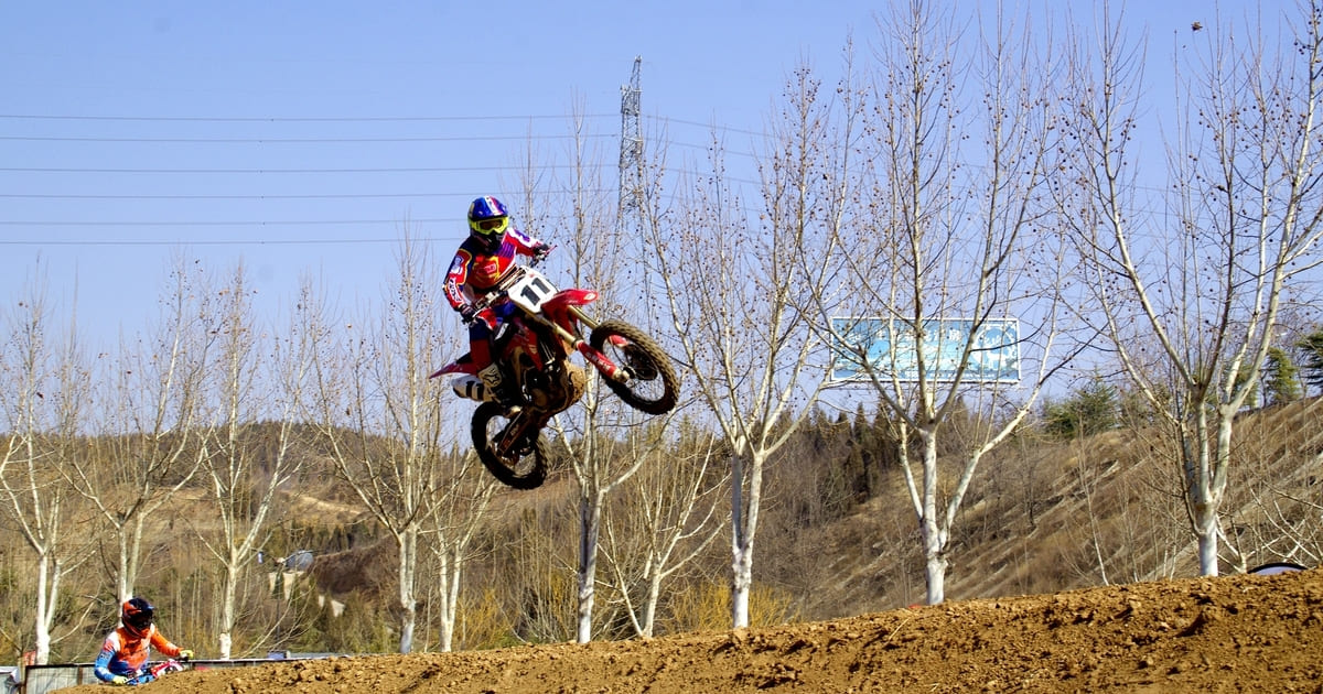 A motocross rider jumps a dirt bike on a track, showcasing the importance of dirt bike weight in maintaining control and balance