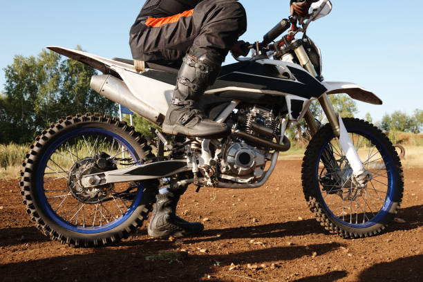 A motocross rider in full gear preparing to kick start a dirt bike outdoors.