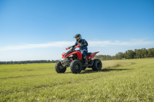ATV rider leaning into a turn on flat ground, demonstrating proper riding technique for beginners, with a grassy field and blue sky in the background.