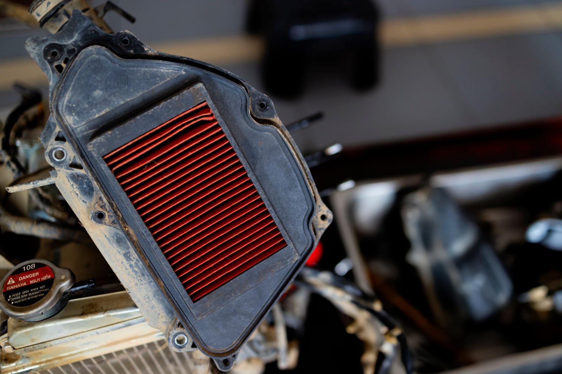 Cleaning and oiling a dirt bike foam air filter on a workbench with cleaner and filter oil
