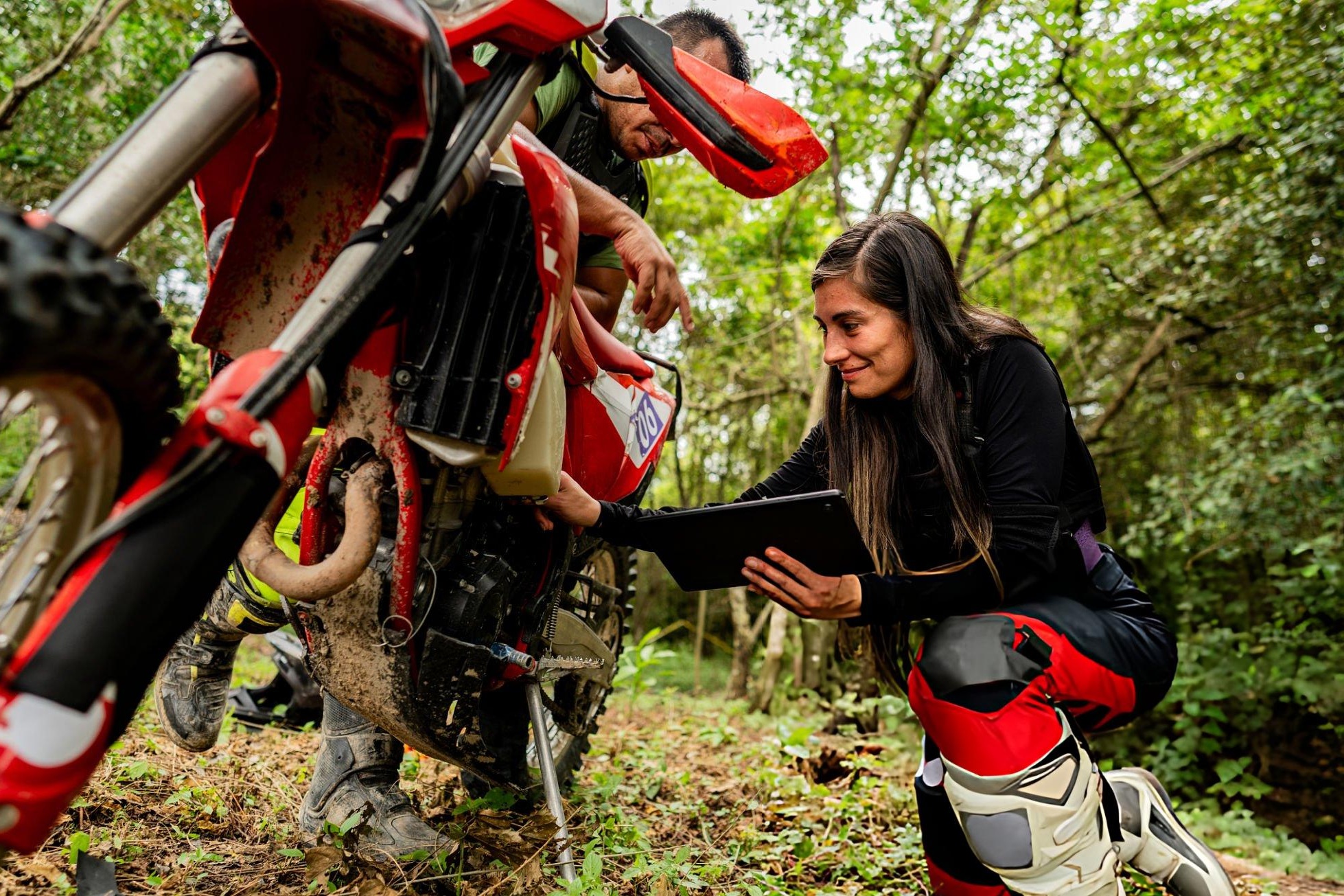 Beginner performing a pre-ride dirt bike inspection with a checklist before trail riding