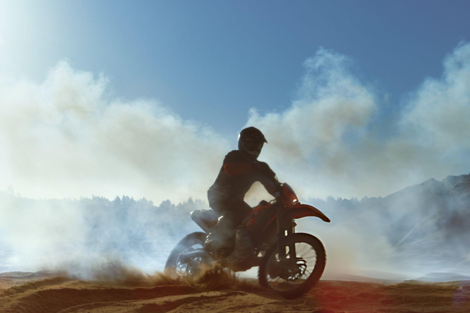 Dirt bike overheating on a forest trail with steam from the radiator while the rider checks the cooling system