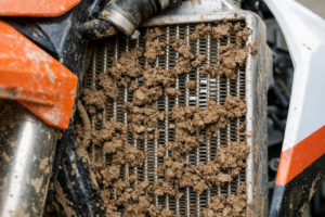 Close up of a dirt bike radiator clogged with mud and debris showing restricted airflow that can cause overheating